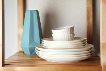 Set of dinnerware on wooden shelf against light background. Interior element