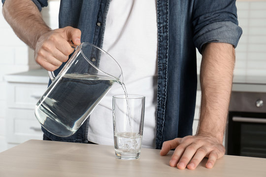 Man pouring water into glass at table, closeup