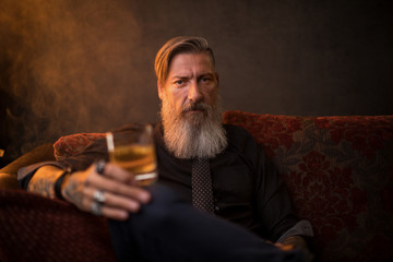 Portrait eines attraktiven Geschäftsmannes mit einer Zigarre und einem Glas Whiskey vor dunklem...