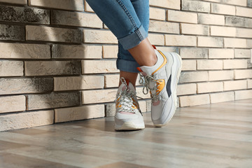 Woman in stylish sneakers near brick wall indoors, closeup