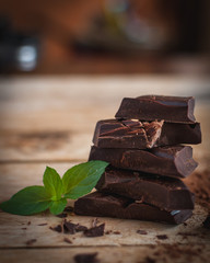 Close-up of stacked dark chocolate with fresh mint on wooden background 