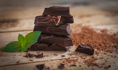 Close-up of stacked dark chocolate with fresh mint on wooden background 