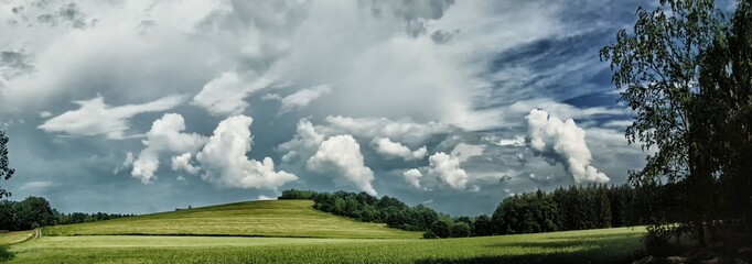 Scenic landscape with storm cloud in background over green agriculture fields,birch tree and meadows at spring daylight. Dramatic storm clouds and sky.Relaxing nature,sushine. Panoramic photo. Czech R