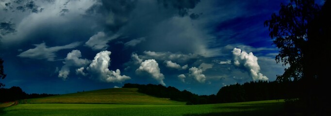 Fototapeta premium Scenic landscape with storm cloud in background over green agriculture fields,trees and meadows at spring daylight, dramatic clouds, sky.Relaxing nature,sunshine.Panoramic photo.Czech Repulic, Europe.