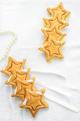 Two rows decorative golden stars handmade from dough on a white fabric surface