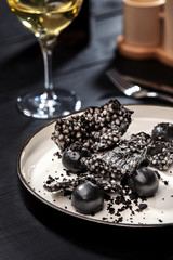 Appetizer with salmon pate, ink cuttlefish, crackers served on white tray over black wooden background. Close-up