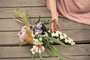 beautiful tender girl in a peach-colored dress sits on a rural wooden bridge with a bouquet of flowers