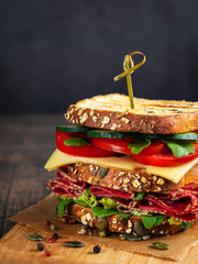 Close-up of delicious Sandwich with salami, cheese and fresh vegetables on rustic wooden cutting board on wooden table, selective focus. Space for text. Vertical. Club sandwich concept.