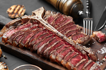Sliced Steak T-bone lying on wooden board. Grilled vegetables in a pan grill. Black background. Close-up