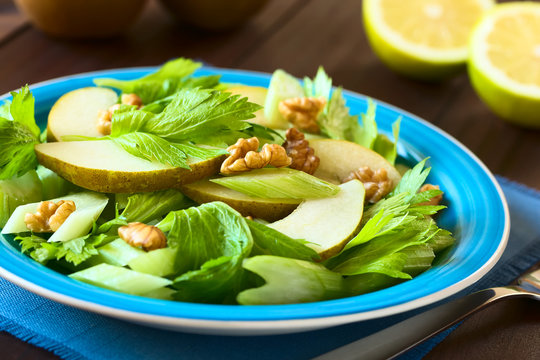 Fresh celery, pear and walnut salad on blue plate, with half lemons in the back, photographed with natural light (Selective Focus, Focus in the middle of the image)