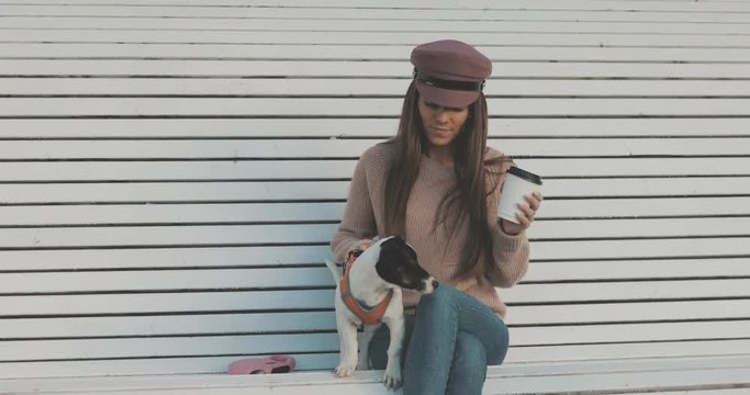 Pretty caucasian woman with dog jack russell terrier sitting on bench and drinking coffee. Cute little puppy 4K video shooting