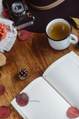  Flat lay view of autumn leaves and tartan textured sweater on wooden background with cup of tea . Autumn or Winter concept.