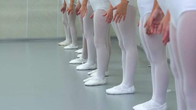 closeup legs of little ballerinas group in white shoes in row practicing in ballet school slow motion. Young girls training elements of classical dance exercise. Childhood, dancing, lifestyle concept