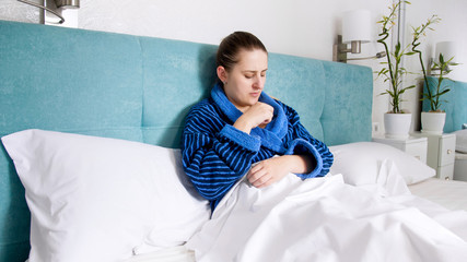 Portrait of sick woman lying in bed and taking digital thermometer under the arm