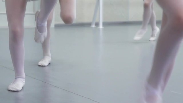 closeup legs of little ballerinas group in white shoes practicing in ballet studio, slow motion. Young girls training elements of classical dance exercise. Childhood, dancing, lifestyle concept