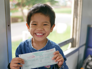 Little Asian baby, 32 months old, holding a train ticket in her hands with big happy smile while she is traveling by train for the first time in her life