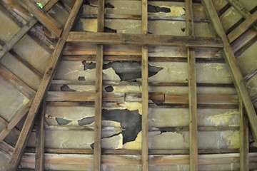 Closeup photograph of the underside of a damaged roof of a pergola showing a timber roof truss and cracked asbestos plates.