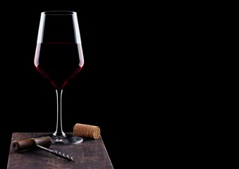 Fotobehang Glass of red wine with vintage corkscrew opener and cork on wooden board on black background. Space for text © DenisMArt