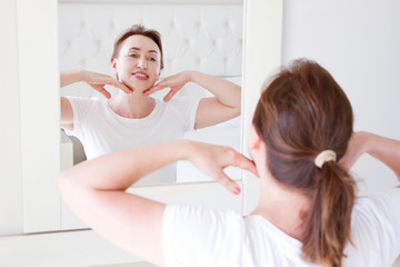 Middle age woman looking in mirror on face. Wrinkles and anti aging skin care concept. Selective...