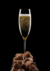 Elegant glass of yellow champagne with corks on black marble board on black background.