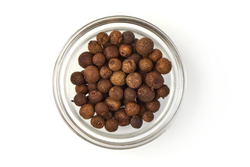 Dried whole allspice in a transparent cup, isolated on white background. Close-up. Top view.