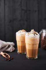 Iced caramel latte coffee in a tall glass with chocolate syrup and whipped cream. Dark wooden background with copy space.