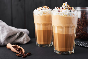Iced caramel latte coffee in a tall glass with chocolate syrup and whipped cream. Dark wooden...