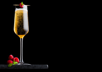 Elegant glass of yellow champagne with raspberry and fresh berries with mint leaf on stick on black...