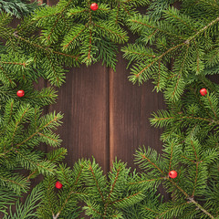 Fototapeta na wymiar Christmas greeting card frame with place for your text. Decorations of green fir branches, reds berries against a background of brown old worn wooden boards