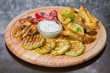 vegetarian grill with zucchini, french fries, mushrooms, paprika, white sauce and dill on wooden plate, closeup food photo