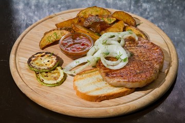 Grilled chicken meat with pickled onions and zucchini, fried potatoes, served on wooden plate, beautiful food photo