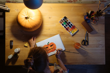 Girl draws a pumpkin at a wooden table
