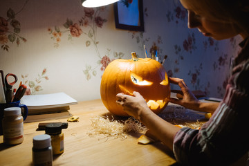 halloween, decoration and holidays concept - close up of woman with knife carving pumpkin or jack-o-lantern at home