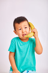 A child boy in a turquoise shirt, holds a banana in place of a phone while talking about a conversation - fruits and a healthy diet