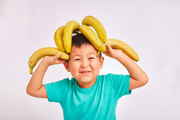 Child boy in a turquoise shirt, head on bananas - fruit and healthy food