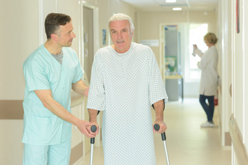 male doctor is helping old man with crutches