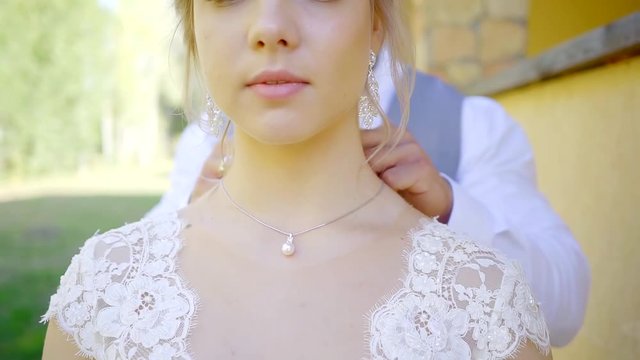 groom is putting golden chain with white pearl on neck of his young bride and fastening, woman is looking