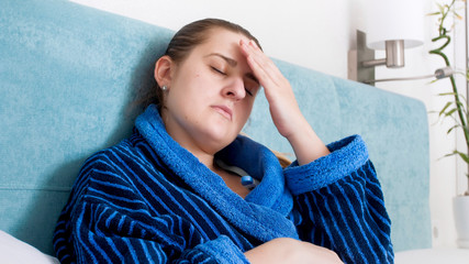 Portrait of young sick woman suffering from fever and head ache lying in bed
