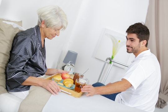 Young man serving breakfast in bed to elderly lady