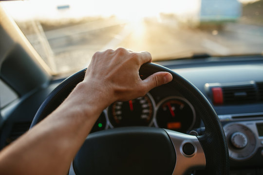 Selective focus man's hand on steering wheel, driving a car at sunset. Travel background