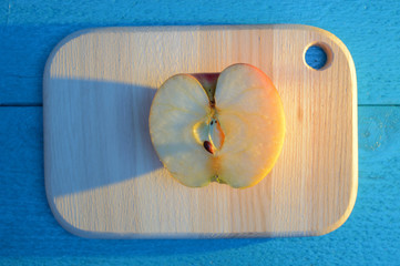 apple cuted in half on a wooden board on turquoise table with a long blue shadow