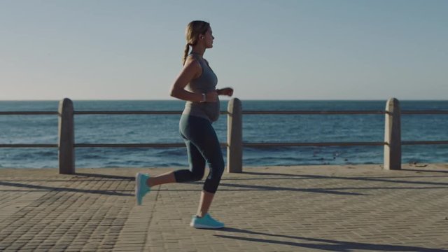 young pregnant woman running exercising healthy active lifestyle using earphones listening to music jogging in seaside at sunrise slow motion