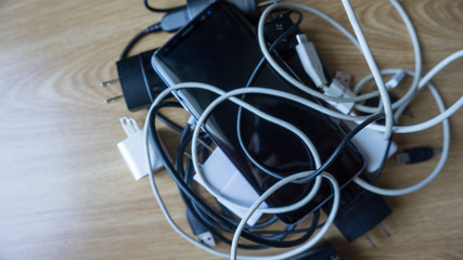 Smartphone tangled in differnt electronics cables chargers usb 7 black and white wires. With copy empty blanck space