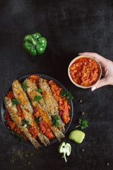 Fried fish in a plate with  tomato sauce, greens and peppers on dark background