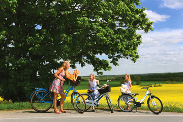 Obraz premium A young mother and her twins take a break from their bicycle ride to view the countryside's scenery. The beautiful view is of the rolling landscape and yellow rapeseed fields that lay before them.