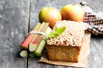 Homemade  apple cake topped with rhubarb jam and sweetened oats on wooden table