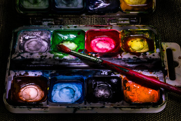 Old used watercolor paint box and brush close - up macro still life.