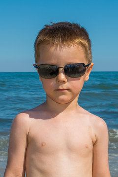 a beautiful little boy posing on a beach by the sea with sunglasses