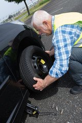 Fototapeta na wymiar aged man changing leaking tire on the verge