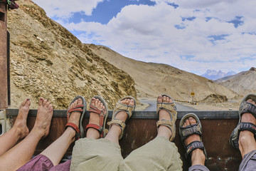Feet of four hitchhiking people laying on the moving truck body in Himalaya mountains, Kashmir, India. - Powered by Adobe
